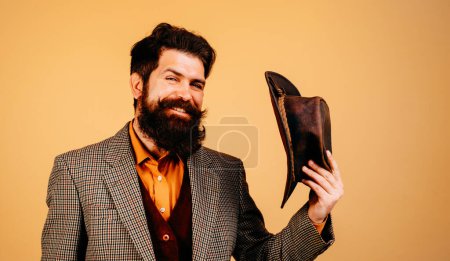Photo for Cheerful smiling gentleman takes off hat in salutation isolated at orange background. Handsome bearded polite man is happy to see someone. Men style and manners concept - Royalty Free Image