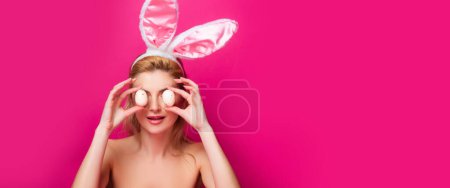 Foto de Una mujer encantadora disfrazada de conejo. Hermosa chica con orejas de conejo y huevos de Pascua sobre fondo rosa. Banner de foto horizontal para el diseño del encabezado del sitio web - Imagen libre de derechos