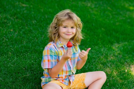 Photo for Summer cute kid face. Strawberries for kids. Child eat strawberry on summer green grass background - Royalty Free Image