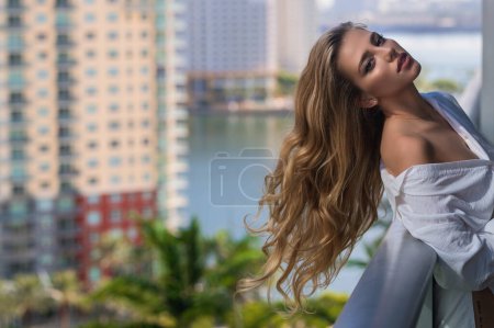Téléchargez les photos : Sexy woman on terrace. Young lady in stylish shirt poses on balcony and enjoys spring. Girl on terraced house by the sea, enjoy morning fresh air with ocean. Sensual woman enjoy town view at terrace - en image libre de droit