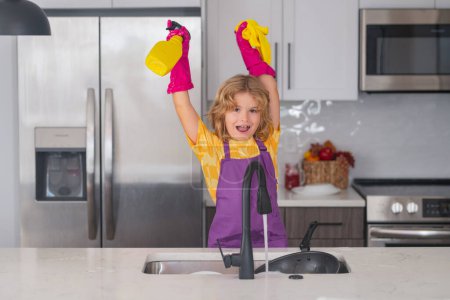Foto de Concepto de lavado y limpieza. Retrato de limpieza infantil en el kithen. Niño ama de llaves lavar los platos con agua jabonosa. Lindo chico divertido lavando platos en la cocina - Imagen libre de derechos