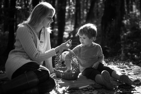 Foto de Joven madre dando a su pequeño hijo una dulce berrie temporada en el picnic de otoño. Mamá y el niño sentados en la manta de picnic y comiendo de la cesta de picnic. Día cálido soleado otoñal. Concepto familiar - Imagen libre de derechos
