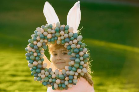 Téléchargez les photos : Enfant garçon avec oeufs de Pâques et oreilles de lapin en plein air. Enfant mignon ayant Pâques heureux dans le parc. Enfants drôles visage gros plan - en image libre de droit