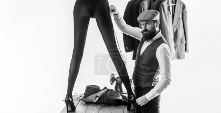 Photo for Long sexy woman legs in black tights. Atelier worker flirting with female. Handsome bearded apparel cutter designer man taking measurements from sexy hot beautiful girl - Royalty Free Image