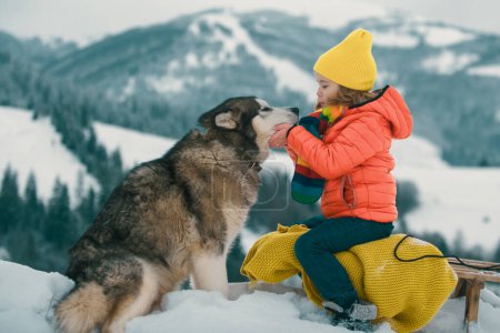 Foto de Niños de invierno con perro Husky en la nieve. husky siberiano con ojos azules en el bosque de invierno, Austria o Canadá - Imagen libre de derechos