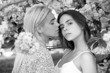 Photo for Young girls and spring flowers. Portrait of a two beautiful young women relaxing in sakura flowers. Lesbian couple kissing. Sensual touch and kiss. Girlfriends couple - Royalty Free Image