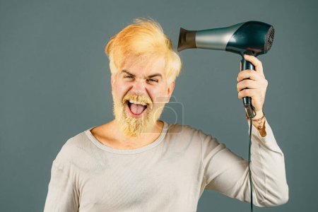 Téléchargez les photos : Cheveux blonds plus secs pour un hipster barbu. Blonde Homme avec sèche-cheveux, sèche-cheveux ou fen - en image libre de droit