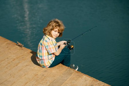 Foto de Pescador de niños pequeños. Pesca infantil en la orilla del río, actividad de ocio al aire libre de verano. Niño en la orilla del río con caña. Pescado - Imagen libre de derechos