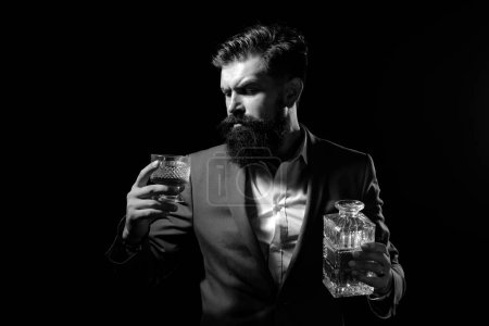 Téléchargez les photos : Whisky élégant. Un homme barbu tient un verre de brandy. Homme d'affaires barbu en costume élégant avec un verre de whisky. Concept de boisson de luxe - en image libre de droit