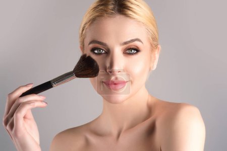 Téléchargez les photos : Beautiful young woman apply powder on face. Beauty Makeup. Portrait of female model with cosmetic brush. Perfect soft skin and natural makeup. Applying powder blush highlighter, foundation tone - en image libre de droit