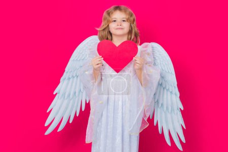 Photo for Kid angel with heart symbol love and valentines day. Little angel. Portrait of cute kid with angel wings isolated on red studio background. Little angel, valentines day. Angelic kids - Royalty Free Image