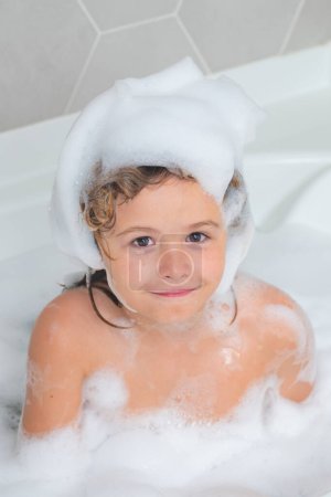 Photo for Sweet blond boy playing with foam in bathtub. Happy kid smiling and looking at the camera. Carefree childhood. Little boy takes a bath with a large amount of foam - Royalty Free Image