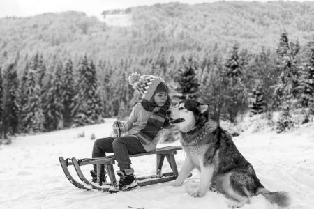Foto de Feliz niño de invierno. Perro alaskan malamute y cabrito en nieve invierno, Austria o Canadá - Imagen libre de derechos