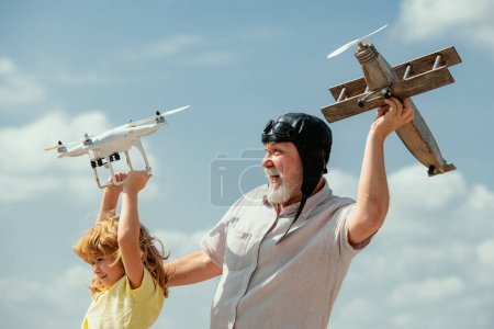 Photo for Grandfather and grandson with plane and quadcopter drone over blue sky and clouds background. Elderly old relative with child - Royalty Free Image