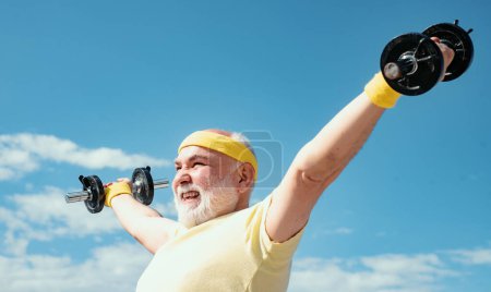 Photo for Old mature man exercising with dumbbell. Senior sportman exercising with lifting dumbbell on blue sky background. Isolated, copy space - Royalty Free Image