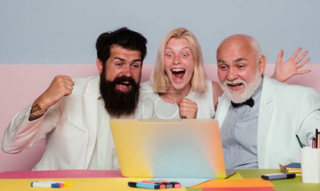 Foto de Successful entrepreneurs and business people. Funny excited group of businesspeople working on a laptop at a table in an office - Imagen libre de derechos