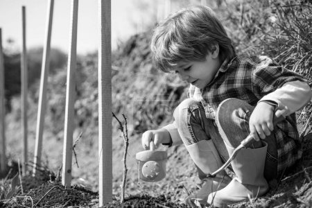 Foto de Niño feliz con pala y regadera. Riego de flores en el jardín - Imagen libre de derechos