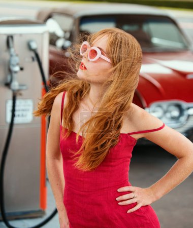 Foto de Gasolinera. Una mujer guapa repostando el auto. Elegante dama contra rojo retro automóvil - Imagen libre de derechos
