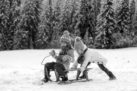 Foto de Niños divertidos en paseo de nieve en trineo. Juegos de invierno al aire libre. Feliz Navidad concepto de vacaciones familiares. Los niños disfrutan de las vacaciones - Imagen libre de derechos