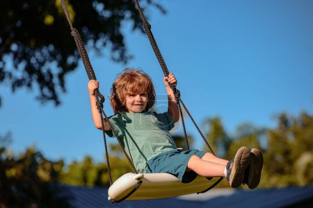 Foto de Un columpio infantil en el patio trasero. Un chico jugando al aire libre. Feliz lindo niño balanceo y divertirse saludable actividad de vacaciones de verano - Imagen libre de derechos