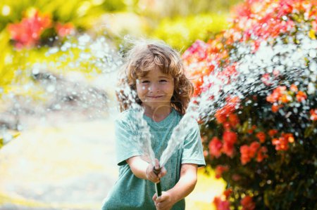 Foto de Divertido niño jugando con manguera de jardín en el patio trasero. Niño divirtiéndose con spray de agua. Actividad al aire libre de verano para niños - Imagen libre de derechos
