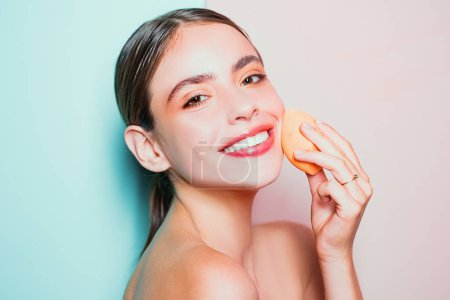 Photo for Healthy smiling girl with bare shoulders, clear skin, dark hair and beige sponge. Natural makeup look. Health and beauty concept. Beautiful young woman apply foundation with beauty blender - Royalty Free Image