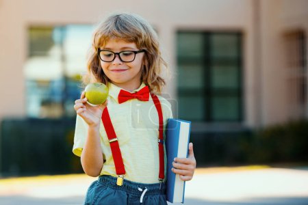 Photo for Portrait of cute school boy with glasses and a shirt with holds book. Schoolkid nerd outdoors - Royalty Free Image