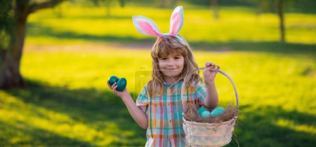 Téléchargez les photos : Joyeuses Pâques pour les enfants. Enfants dans les oreilles de lapin sur la chasse aux œufs de Pâques dans le jardin. Enfants avec des œufs colorés dans l'herbe. Le gamin joue dehors. Cadre de bannière web panoramique - en image libre de droit