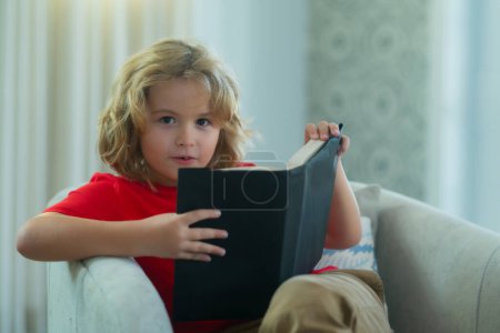 Foto de Kid boy reading book at living room. Concept of education, childhood, book reading and inspiration - Imagen libre de derechos