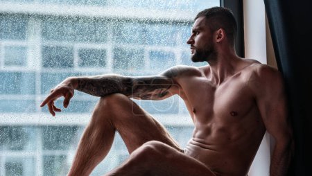 Foto de Handsome muscular man in bedroom on window curtains. Young handsome sexy man resting at home. Guy with athletic muscles. Sexy young handsome naked man on bedroom. Seductive gay - Imagen libre de derechos