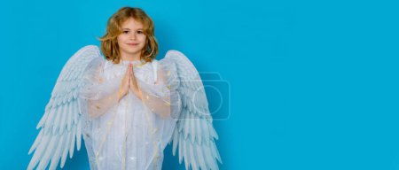Téléchargez les photos : La prière des anges. Saint Valentin. Blonde mignon enfant avec des ailes d'ange sur un fond bleu studio isolé. Bannière pour la conception de l'en-tête, modèle de flyer - en image libre de droit