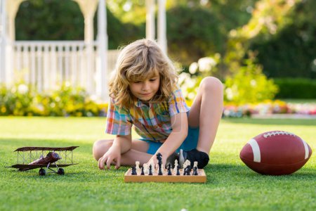 Téléchargez les photos : Enfant développant une stratégie d'échecs, jouant au jeu de plateau dans la cour, s'allongeant sur l'herbe - en image libre de droit