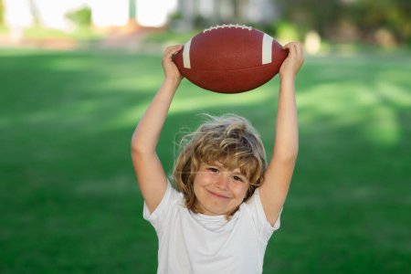 Téléchargez les photos : Football américain. Enfant mignon s'amuser et jouer au football américain sur le parc d'herbe verte - en image libre de droit
