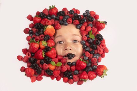 Foto de Healthy vitamins fruits. Berries with kids face close-up. Top view of child face with berri. Berry set near kids face. Cute little boy eats berries. Kid eating vitamins. Close up kids face - Imagen libre de derechos