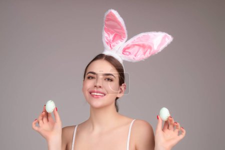 Téléchargez les photos : Photo rapprochée de jolie fille porter des oreilles de lapin pelucheux de Pâques tenir des œufs de Pâques, fond de studio isolé. Portrait mangeur de lapin femelle - en image libre de droit