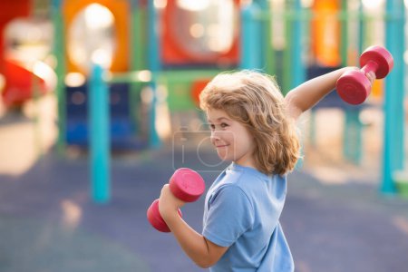 Photo for Kids sport training on playground outdoor. Healthy kids. Sport activities at leisure with children. Blonde boy holding dumbbells. Sports exercises for children. Funny child lifting the dumbbells - Royalty Free Image