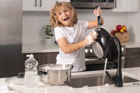 Téléchargez les photos : Child help in washing dishes at kitchen. Clean washed dishes, dishwashing liquid with foam - en image libre de droit
