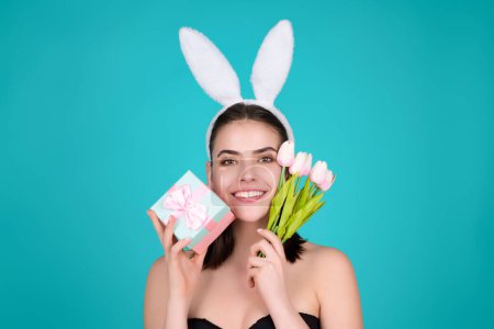Foto de Woman with bunny ears and easter eggs. Easter bunny isolated on studio background. Holidays, spring and party concept. Portrait of lovely, cheerful girl in rabbit ears celebrating Easter - Imagen libre de derechos