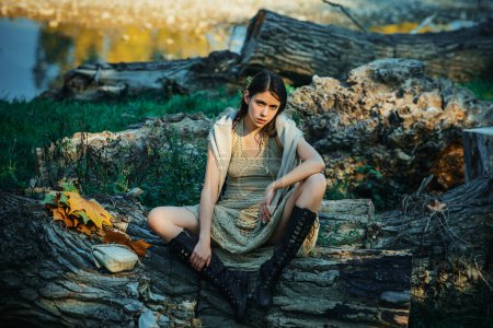Photo for Serious woman on trunk wood. Adult girl relaxed sitting on wood in an outdoor park. Portrait of a beautiful charming young attractive woman in a dress. Girl enjoying nature - Royalty Free Image
