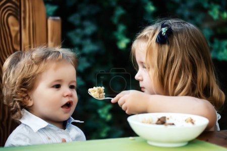 Photo for Sister feeding brother. Girl feeds baby boy with a spoon. Kid food. - Royalty Free Image