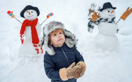 Foto de Niño feliz jugando con bola de nieve sobre fondo blanco de invierno. Retrato de invierno de un niño lindo en la nieve Jardín - Imagen libre de derechos