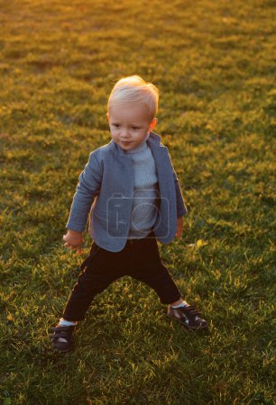 Foto de Niño sentado y jugando con hojas. Lindo niño caminando entre hojas caídas en el parque de otoño. Niño feliz caminando en el parque. Hermoso niño en un suéter gris en la naturaleza de otoño - Imagen libre de derechos