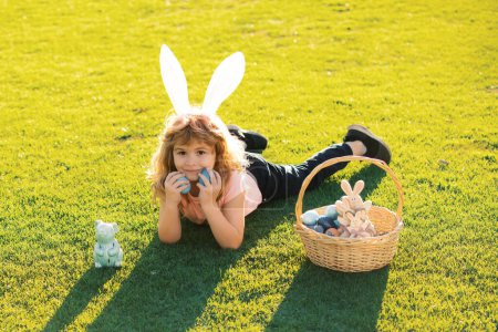 Téléchargez les photos : Enfant garçon avec des œufs de Pâques et des oreilles de lapin posées sur l'herbe. Joyeuses Pâques - en image libre de droit