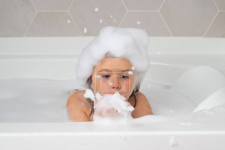 Foto de Children bathing. Boy child in a bath playing with foam, blowing soap. Kids bathing and hygiene procedures - Imagen libre de derechos