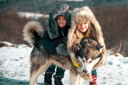 Foto de Niños de invierno abrazan a Husky en la nieve en el bosque de invierno - Imagen libre de derechos