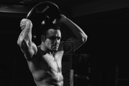Téléchargez les photos : Portrait de powerlifter avec disque de poids dans la salle de sport. bodybuilder avec lourd disque trains son biceps - en image libre de droit