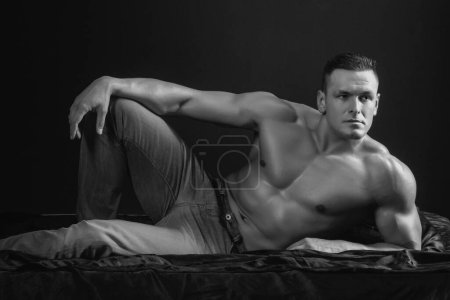 Foto de Retrato joven sexy hombre culturista atleta, con un torso desnudo, se encuentra en una cama en almohadas en ropa interior - Imagen libre de derechos