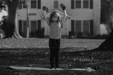 Photo for Kids morning sports exercises. Sport children. Sport child with strong biceps muscles. Kids exercising fitness dumbbells. Strong little boy exercising with dumbbell in park outdoor - Royalty Free Image