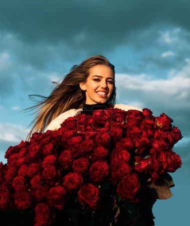 Foto de Joven chica sonriente disfruta de flores de rosas rojas. Concepto de San Valentín. Las mejores ideas del día de San Valentín - Imagen libre de derechos