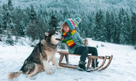 Foto de Feliz niño de invierno. Perro alaskan malamute y cabrito en nieve invierno, Austria o Canadá - Imagen libre de derechos
